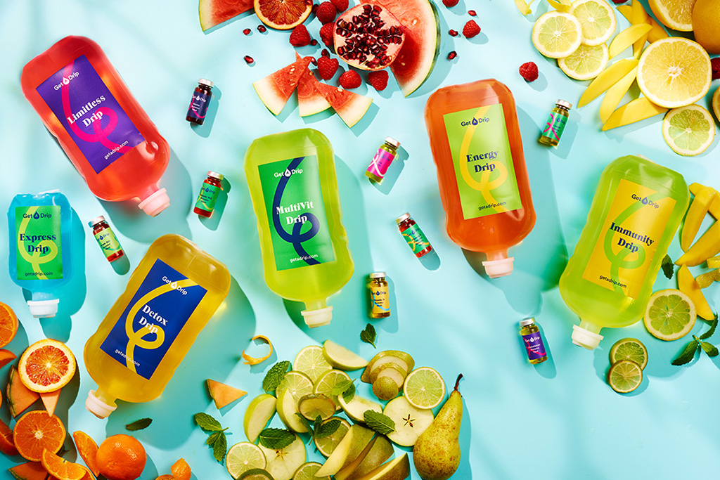 multiple IV Drip bottles and Booster shots on a blue background surrounded by fruit