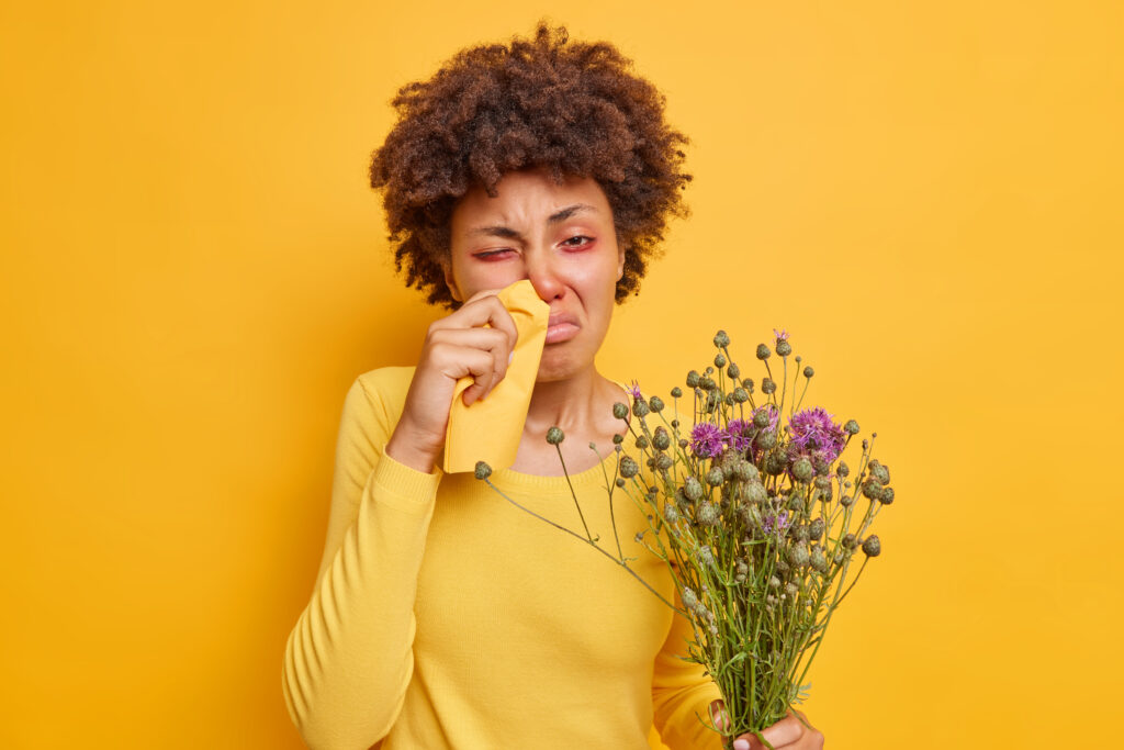 A girl suffering from hay fever with red eyes and a runny nose with a yellow background